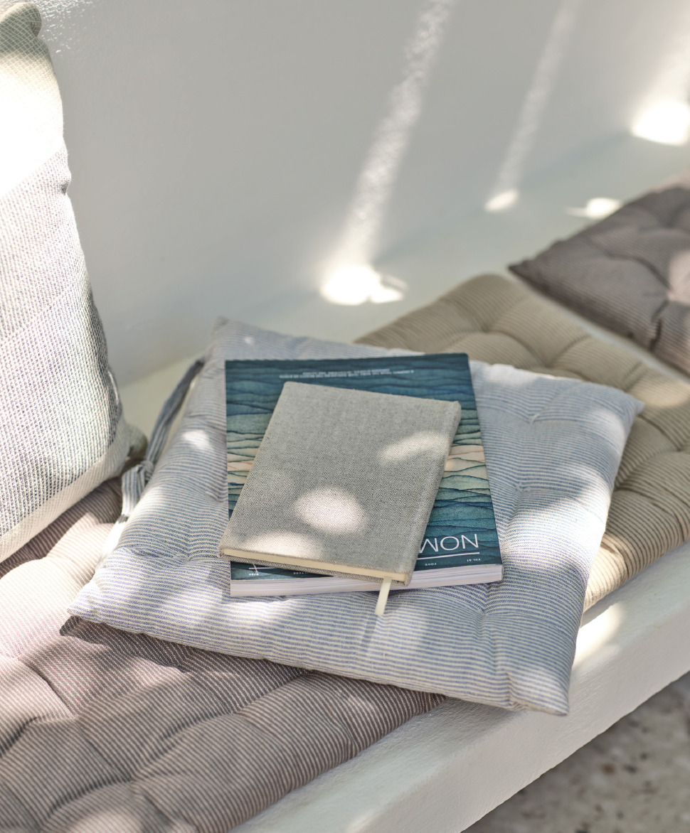 Подушка для садового стільця MYGFJED додає комфорту вашому відпочинку на садовій лаві, де зверху лежать блокнот і книга, створюючи атмосферу спокою та відпочинку.